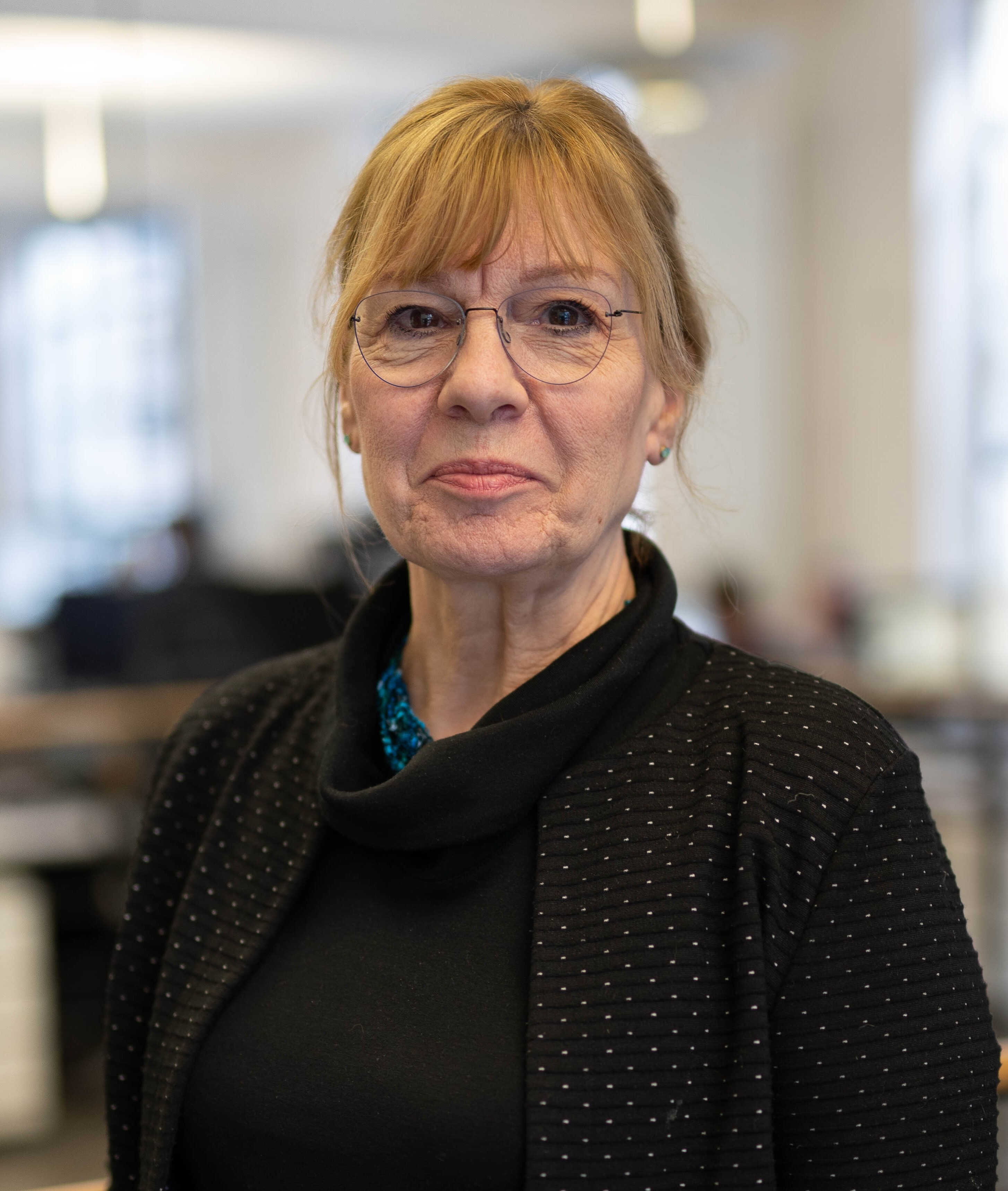 Head & shoulders picture of Jean with her hair up, classes on and a black shirt. She looks down the camera lens