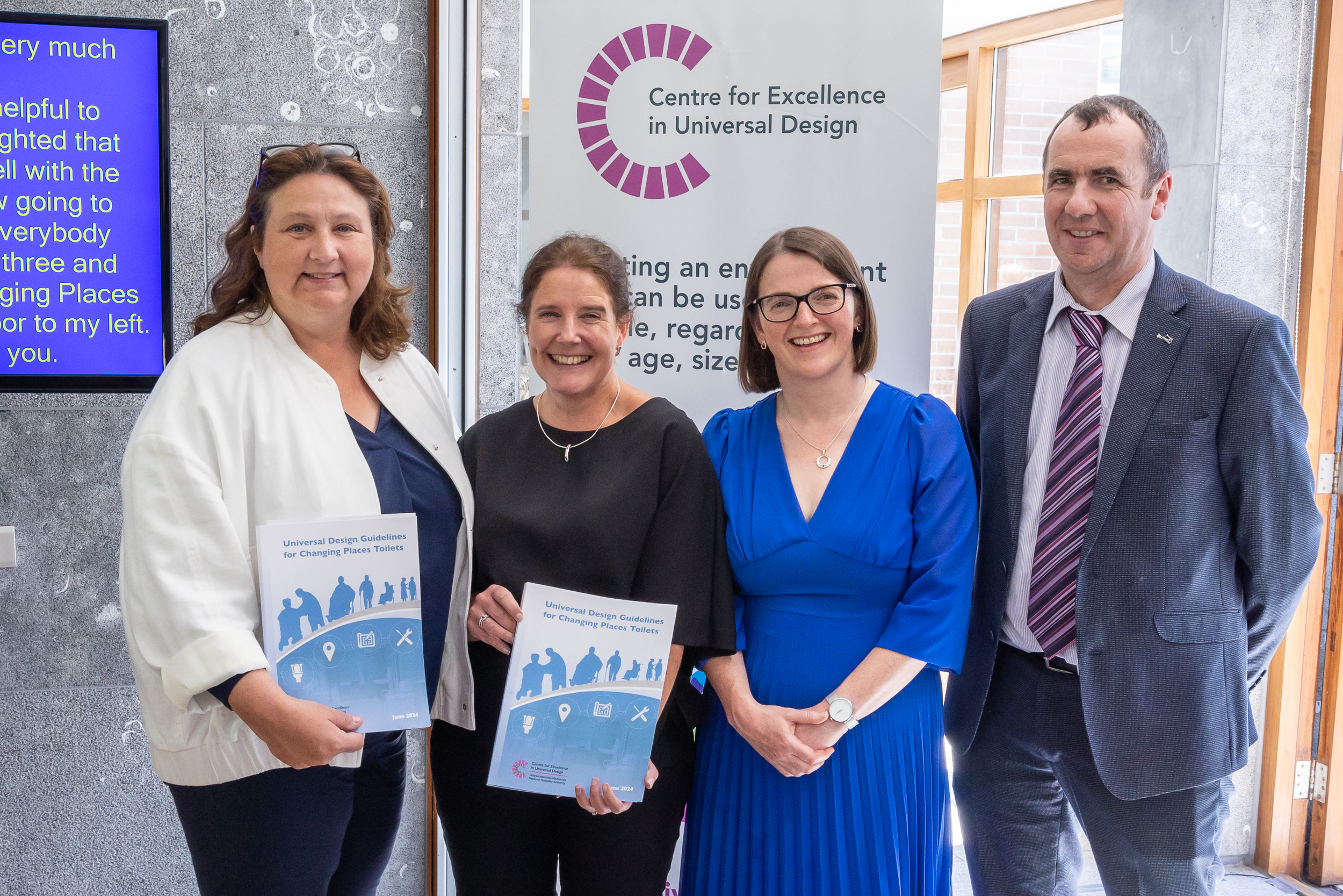 Picture of Anne Rabbitte T.D., Aideen Hartney, Ruth O’Reilly, and Paul McDermott. Anne Rabbitte and Aideen Hartney are holding copies of the new guidelines and they are all standing in front of a Centre for Excellence in Universal Design Banner.